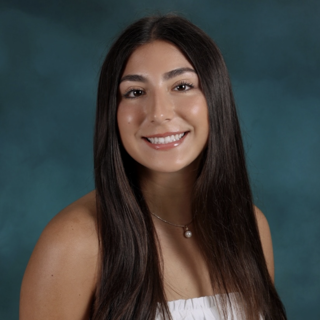 Smiling woman with long dark hair wearing a white top, posed against a teal background.