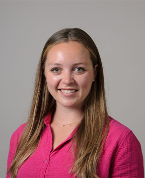 Staff member smiling at the camera in front of a grey background.