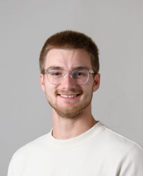 Staff member smiling at the camera in front of a grey background.