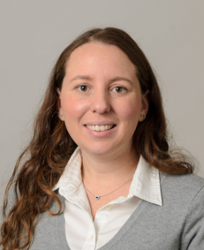 Staff member smiling at the camera in front of a grey background.