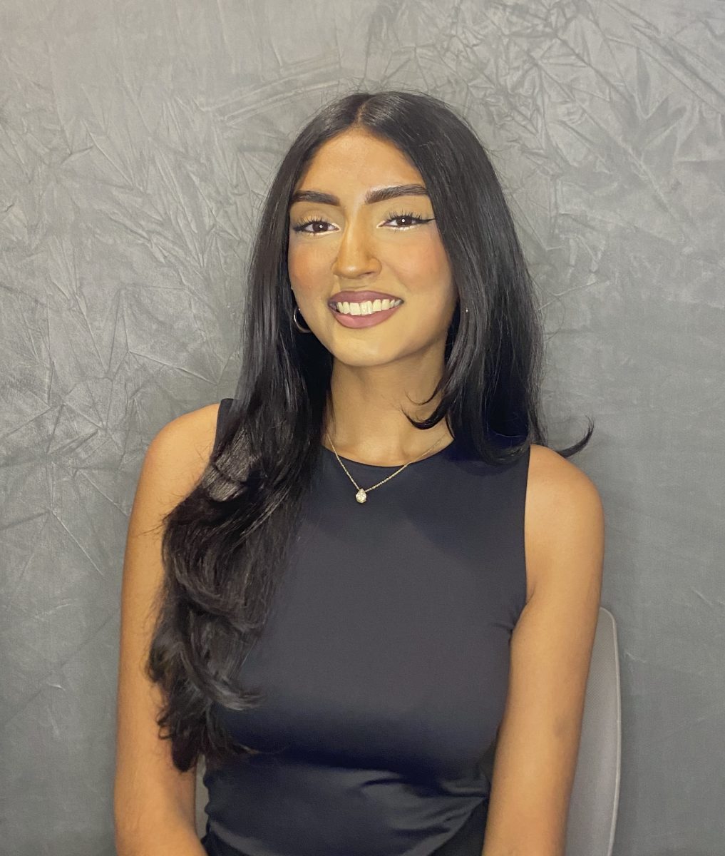 Staff member smiling at the camera in front of a grey background.