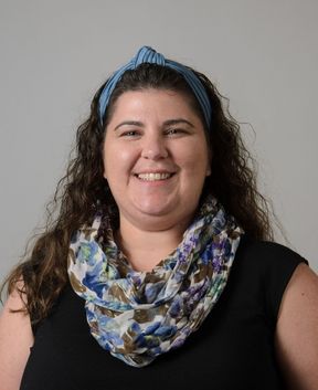 Staff member smiling at the camera in front of a grey background.