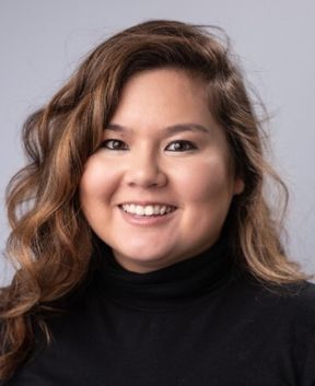 Staff member smiling at the camera in front of a grey background.