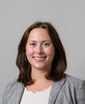 Staff member smiling at the camera in front of a grey background.