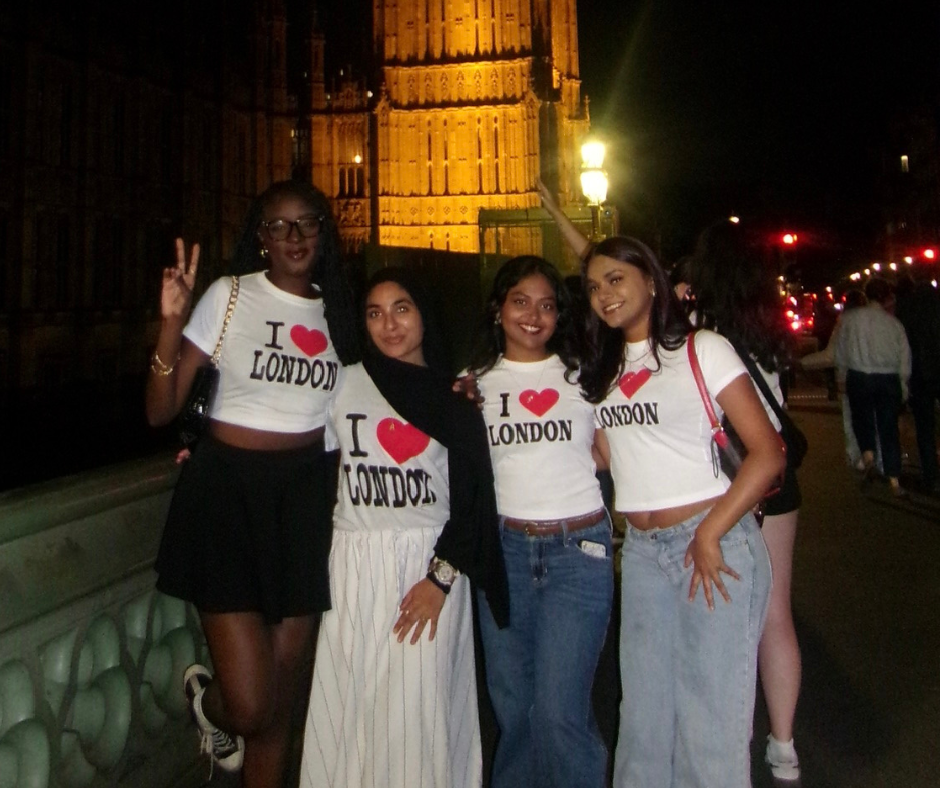 A group of four UConn students pose together at night in front of the illuminated Big Ben clock tower in London. All are smiling and wearing matching "I ❤️ London" T-shirts, representing their study abroad experience.