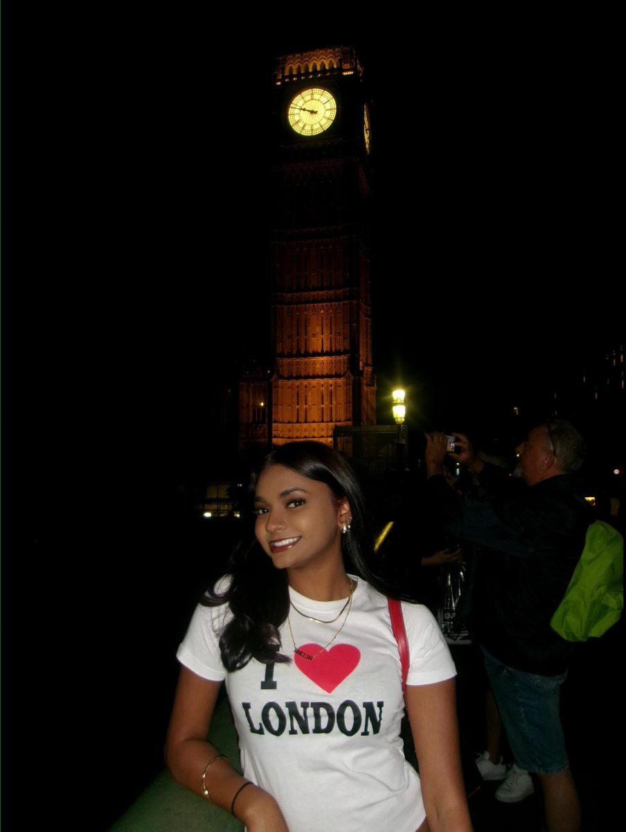 A UConn student smiling in front of Big Ben at night in London. She is wearing a white "I ❤️ London" T-shirt, with the clock tower brightly lit behind her.