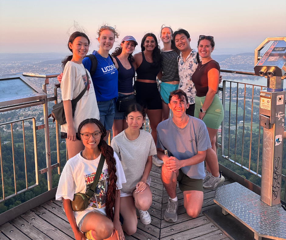 Students posing together on a viewing platform overlooking a city and landscape at sunset during a UConn Global study abroad experience.