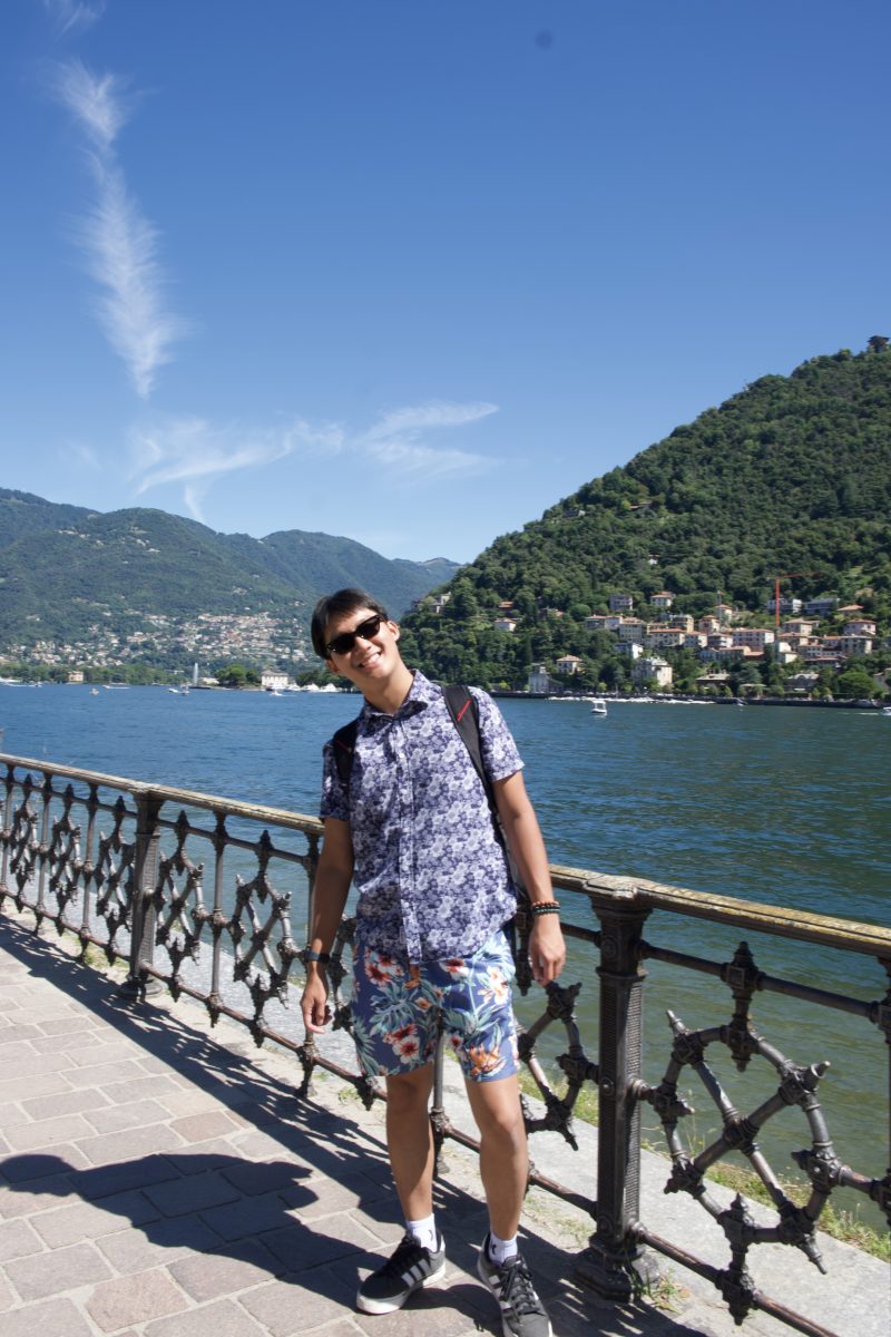 Student smiling by the waterfront with mountains and colorful hillside buildings in the background during a study abroad experience.