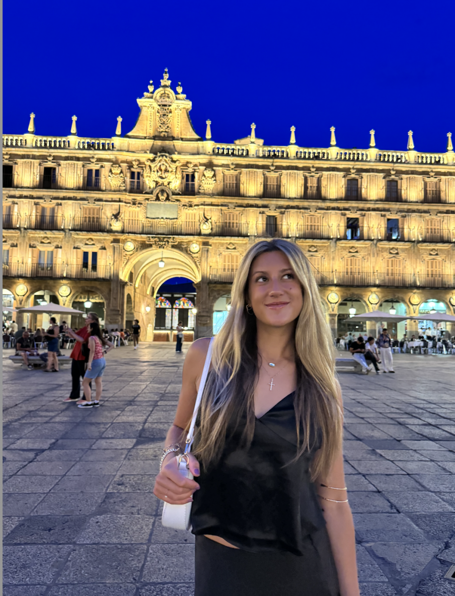 Student smiling in Plaza Mayor, Salamanca, Spain, with the historic city hall illuminated behind her at dusk. The lively square and golden architecture reflect the immersive cultural experiences available through study abroad."
