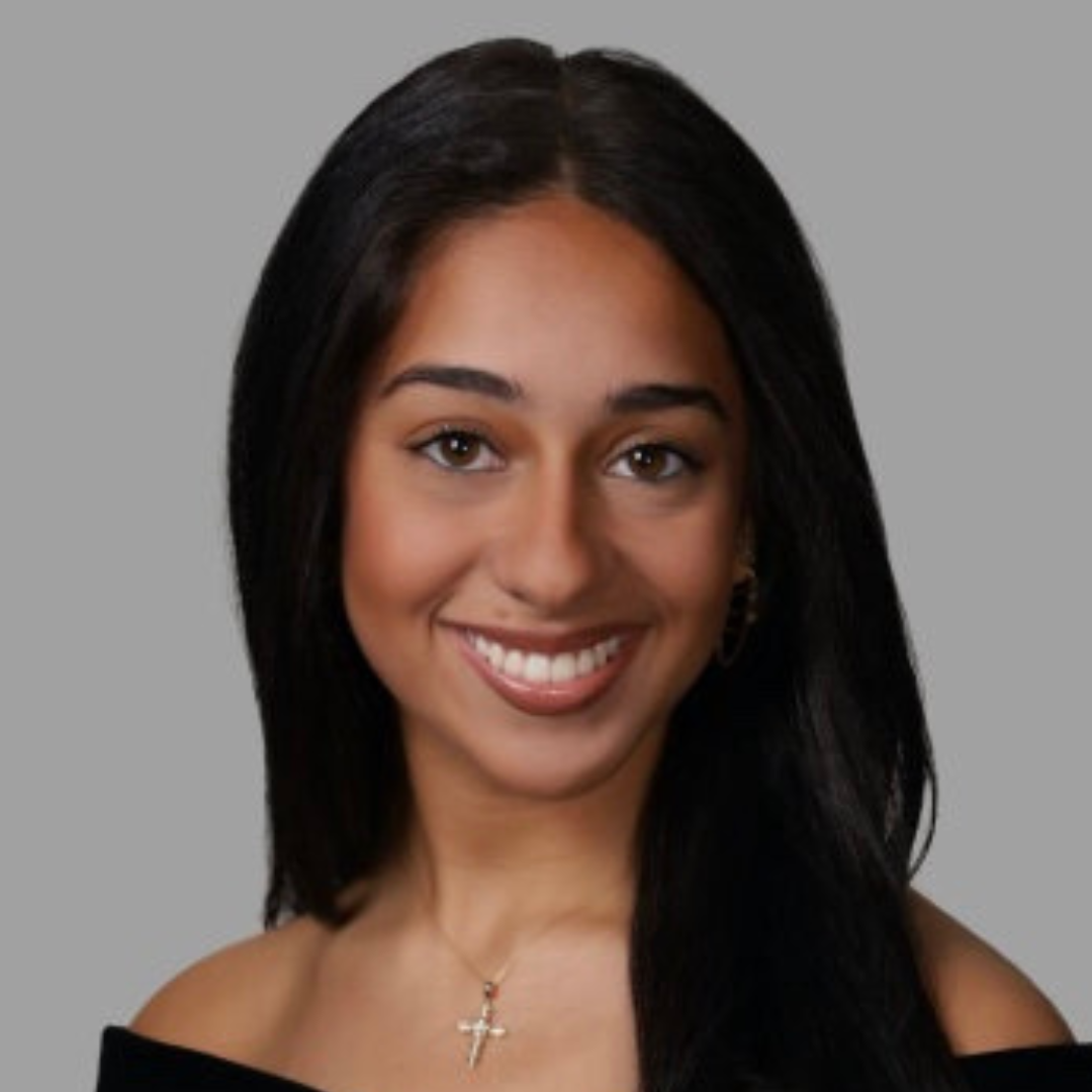 Headshot of UConn student smiling at camera. She has long black hair, and is wearing a black blouse.