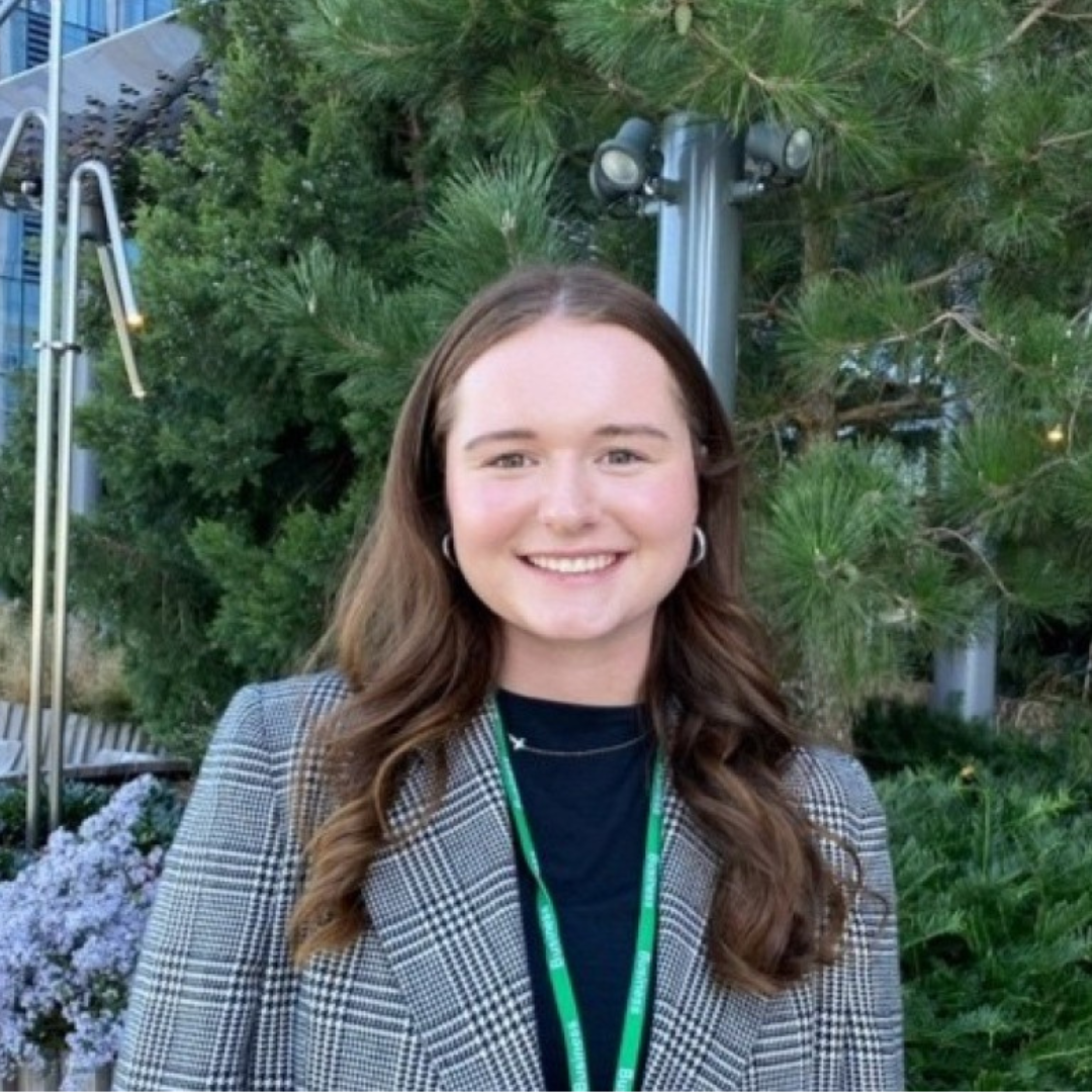 Headshot of UConn student smiling at the camera. She has medium length brown hair, and is wearing a black and white blazer, with a black blouse,