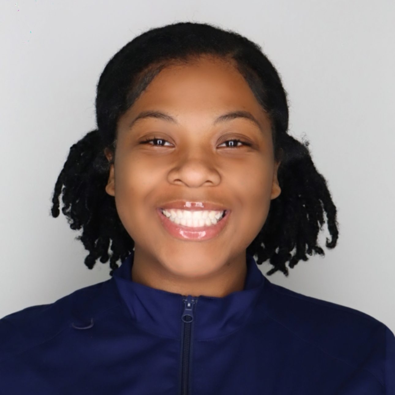 Student is smiling at the camera. She is wearing a UConn School of Nursing zip-up, and has short black hair in pigtails.