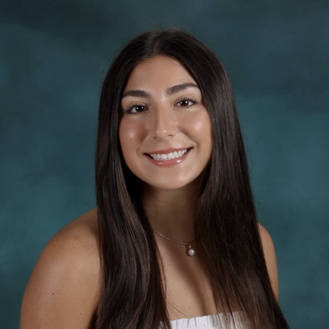 Smiling woman with long dark hair wearing a white top, posed against a teal background.