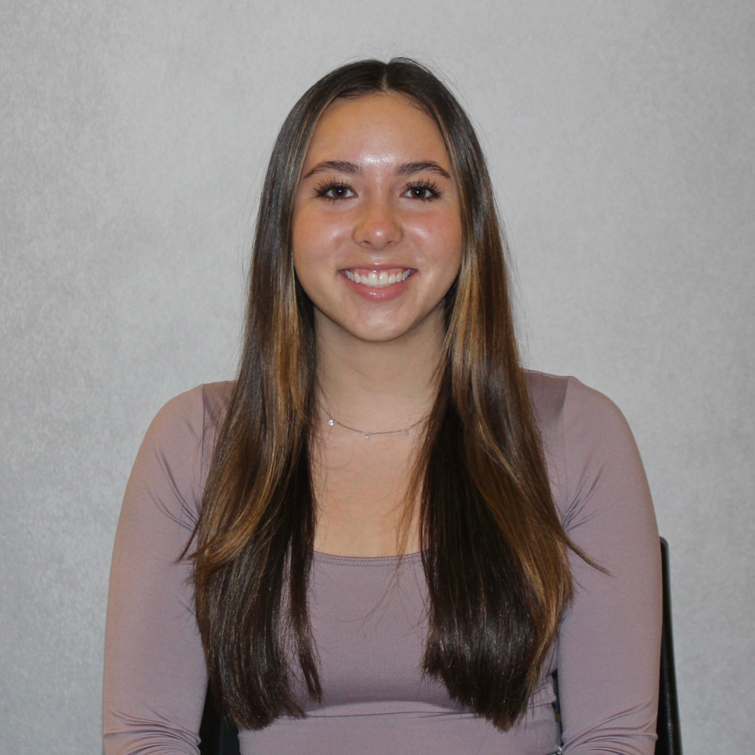 Headshot of UConn student. She has long brown hair, is wearing a mauve long sleeved top, and is smiling at the camera.