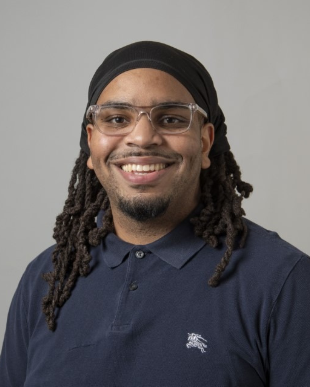 Photo of UConn staff. He is wearing a black polo, and has black dreads with a head covering.